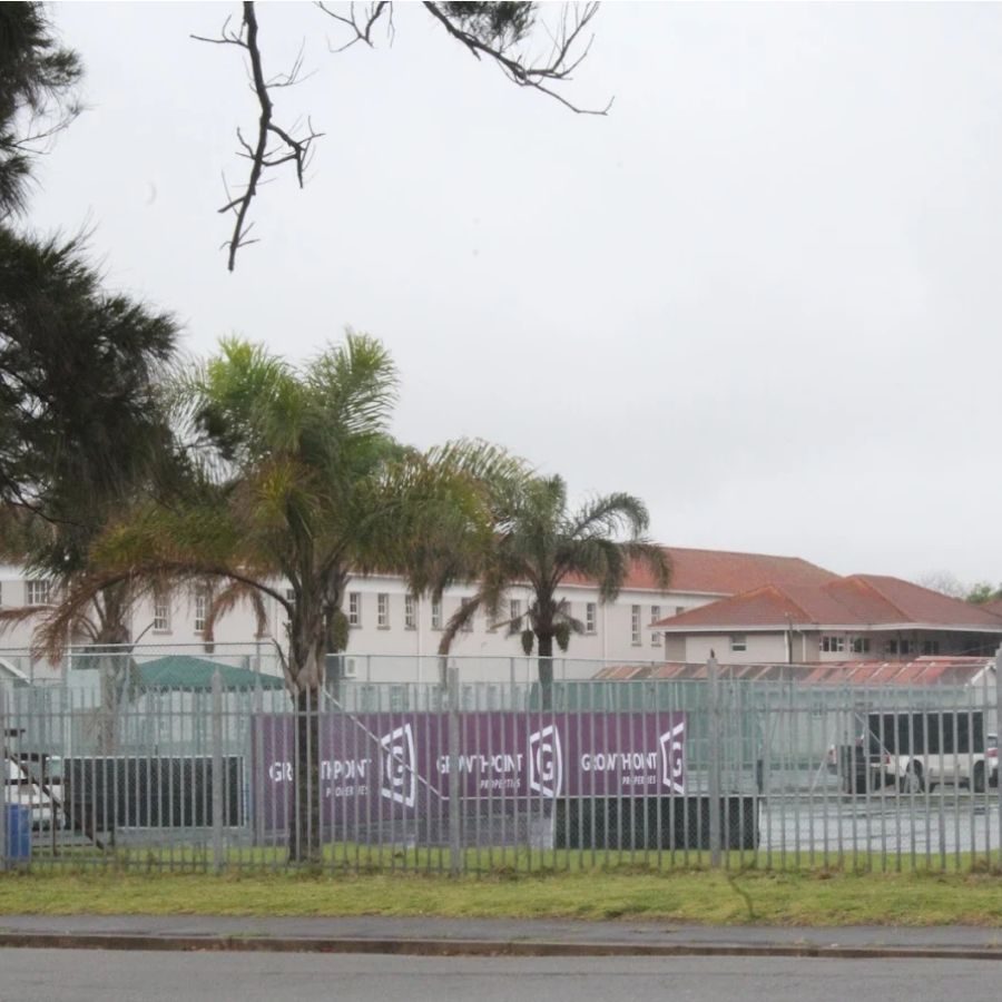 Buffalo City TVET College campus buildings and palm trees viewed through the perimeter fence on an overcast day