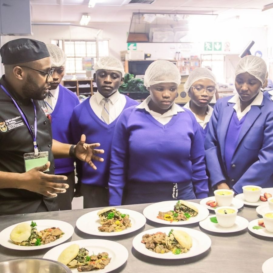 Coastal KZN TVET College culinary students in hairnets reviewing plated dishes with their chef instructor