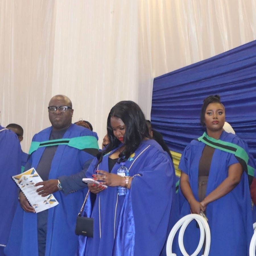 Graduates in Gowns on Ceremony Stage Ehlanzeni TVET College graduates in blue and green academic gowns standing on stage at a graduation ceremony