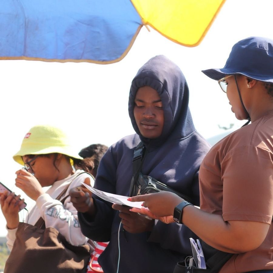 Outdoor Registration at Ekurhuleni West College Event Ekurhuleni West TVET College staff assisting a visitor with paperwork at an outdoor registration point under an umbrella