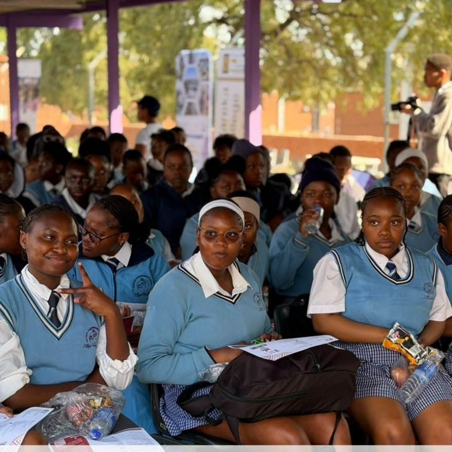 School Learners at Outdoor Recruitment Talk School learners in light blue uniforms seated outdoors listening to an Ekurhuleni West TVET College outreach presentation