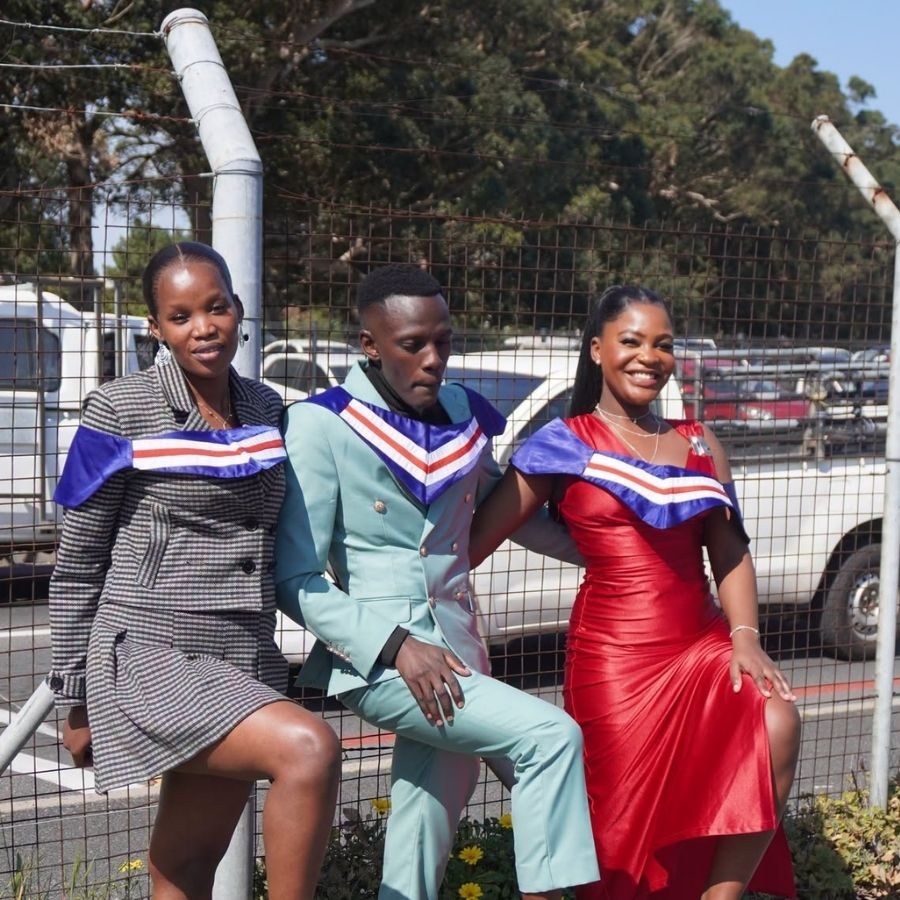 False Bay TVET College Graduates Pose in Sashes Three False Bay TVET College graduates in stylish outfits and blue, white and red graduation sashes posing outdoors together.