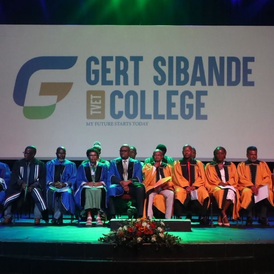 Gert Sibande TVET College Graduation Stage Officials Gert Sibande TVET College officials in blue and gold academic gowns seated on stage beneath the college's illuminated logo.