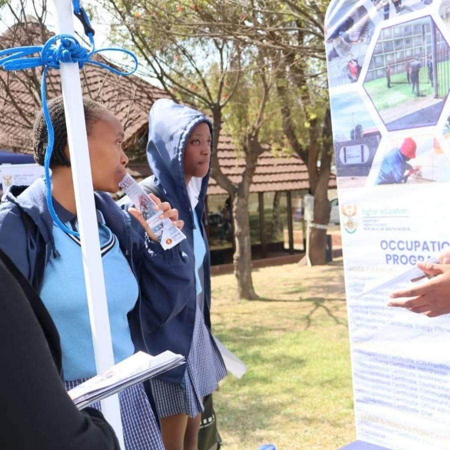 Goldfields TVET College students reading an occupational programmes banner outdoors on campus.