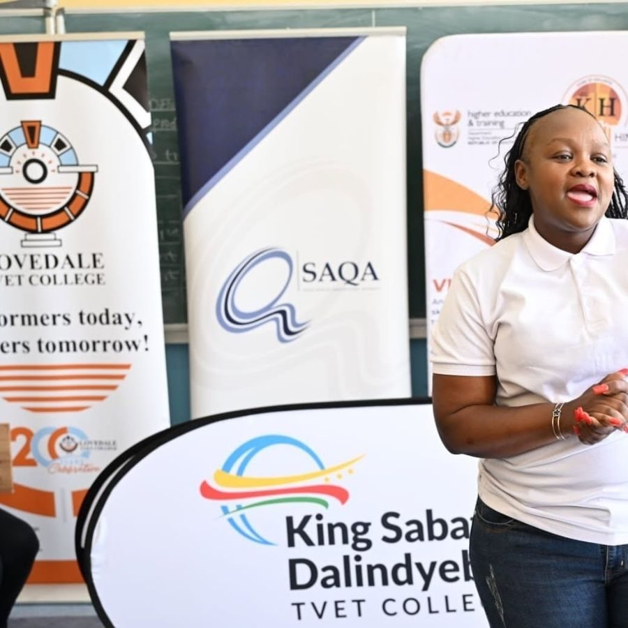 Ingwe TVET College Representative at Sector Forum Speaker at a TVET sector forum, with banners for Lovedale, King Sabata Dalindyebo and King Hintsa TVET colleges behind her.