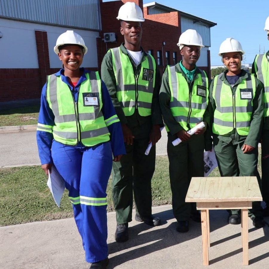 King Hintsa TVET College Construction Trainees Outdoors King Hintsa TVET College construction trainees in hard hats and hi-vis vests walking outdoors with a wooden bench project.