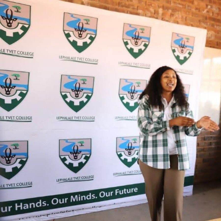Lephalale TVET College Speaker at Branded Event Backdrop Woman speaking in front of a Lephalale TVET College branded step-and-repeat backdrop reading "Our Hands. Our Minds. Our Future"