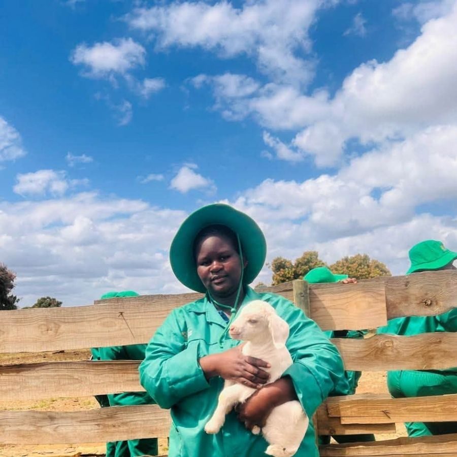 Letaba TVET College Agriculture Student Holding a Lamb Letaba TVET College agriculture student in green overalls and hat holding a lamb at an outdoor livestock kraal