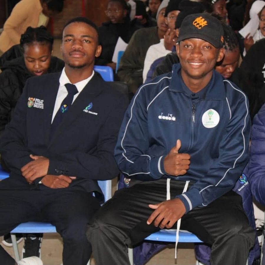 Motheo TVET College Students at Formal Assembly Two Motheo TVET College students, one in a blazer and tie, seated among a crowd at a formal college assembly