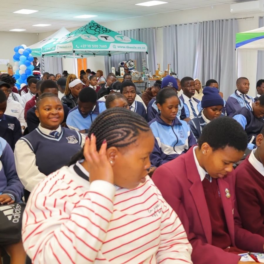 School Pupils Attending an Mthashana College Open Day School pupils in various uniforms seated indoors at an Mthashana College open day with exhibition tents in the background