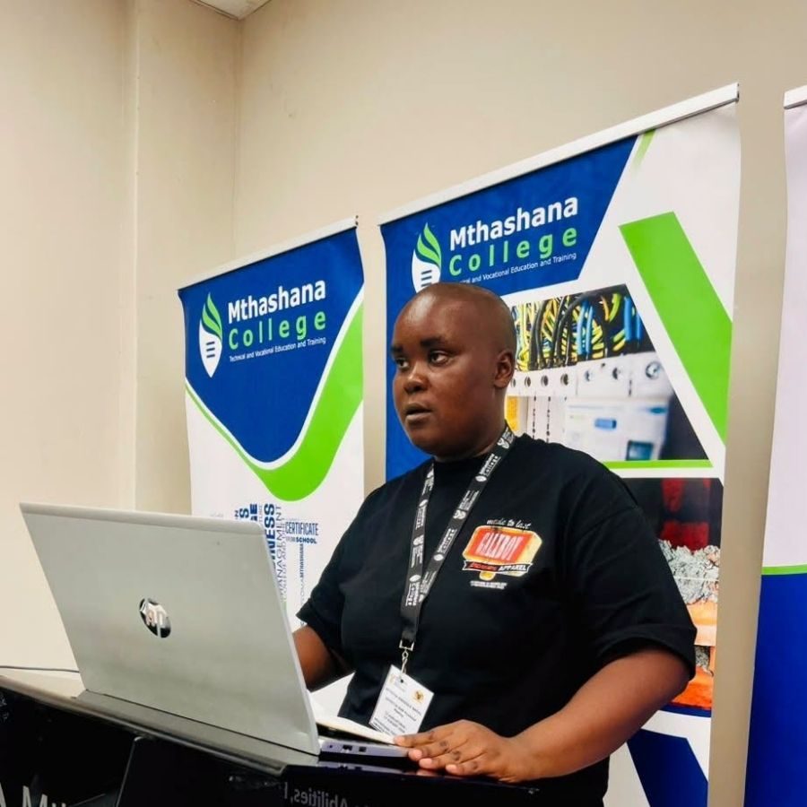 Mthashana College Staff Member Presenting with Laptop Mthashana College staff member standing at a laptop presenting in front of Mthashana College banner roll-ups