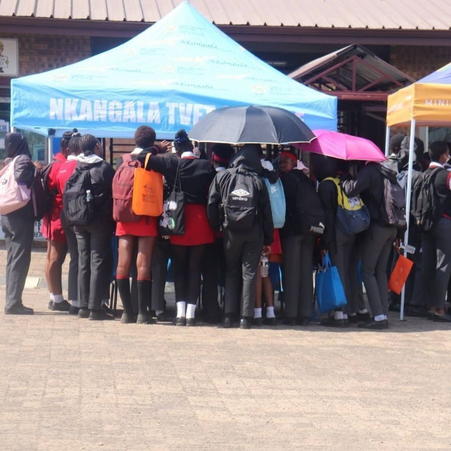 Students Queuing at Nkangala TVET College Open Day Tent Group of students with umbrellas and backpacks gathered at a branded Nkangala TVET College tent on campus