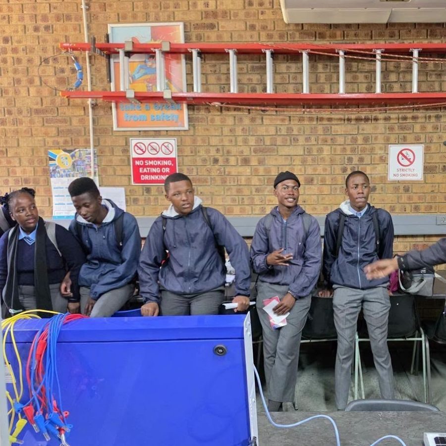 Nkangala TVET College Students in Electrical Training Lab Nkangala TVET College students in grey jackets standing beside a blue electrical training panel in a workshop