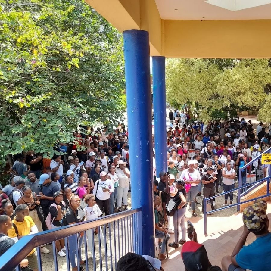 Orbit TVET College Students Queue at Campus A large crowd of Orbit TVET College students and visitors queue outside a campus building under a covered walkway.