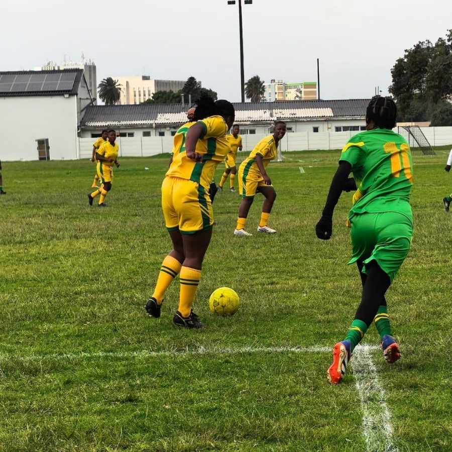 Port Elizabeth TVET College women's soccer players in yellow and green kits compete for the ball.