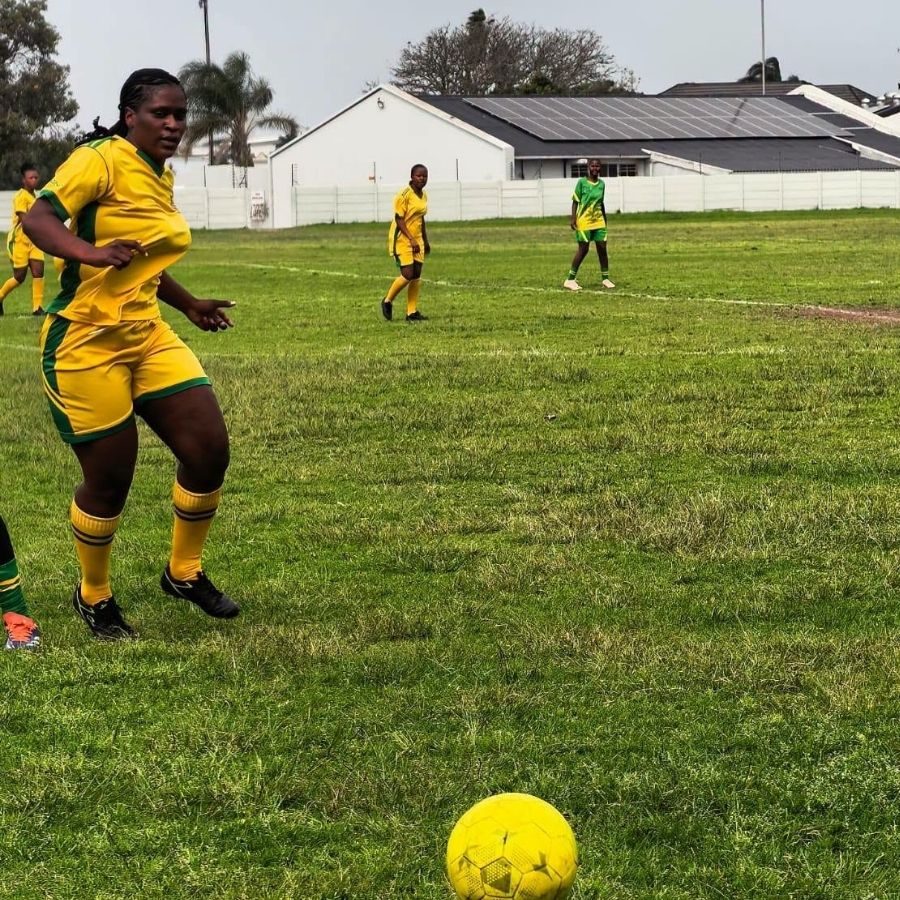 A Port Elizabeth TVET College soccer player in a yellow kit controls the ball during a match.