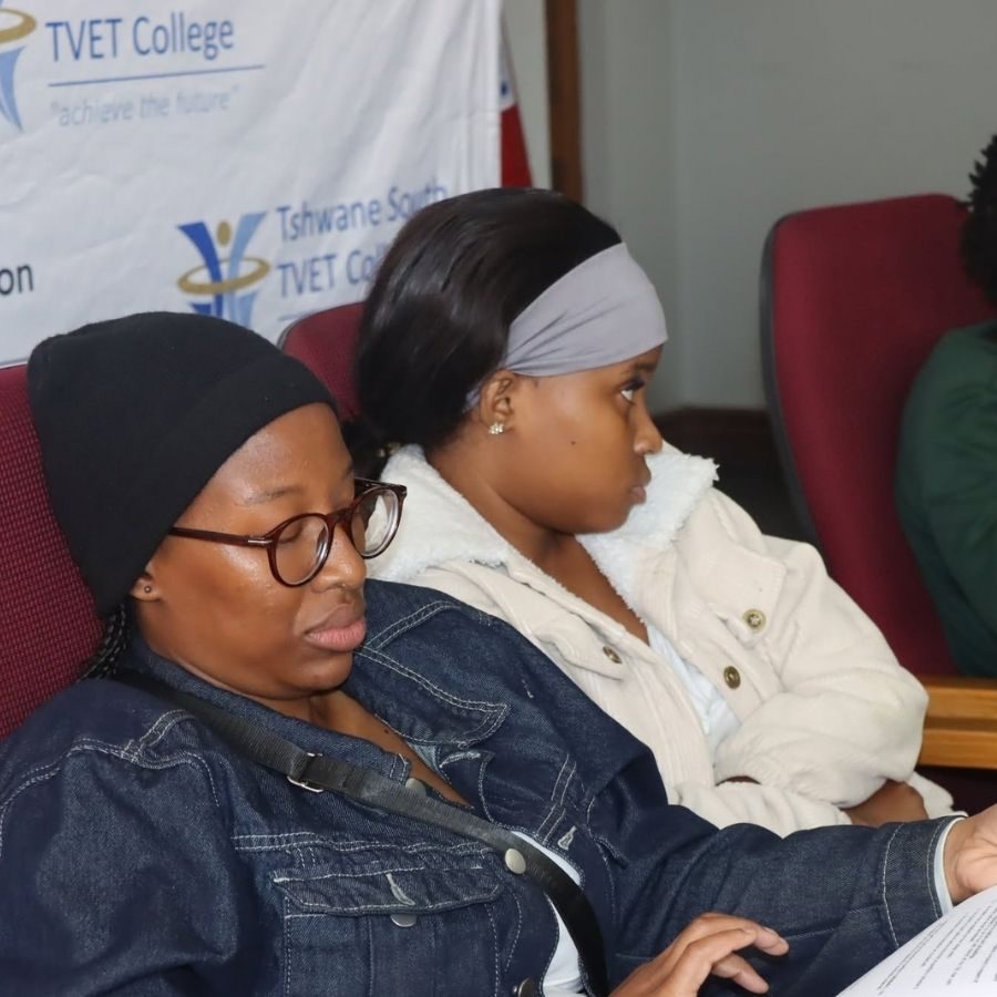 Two Tshwane South TVET College students seated in a hall listening during an orientation or induction session