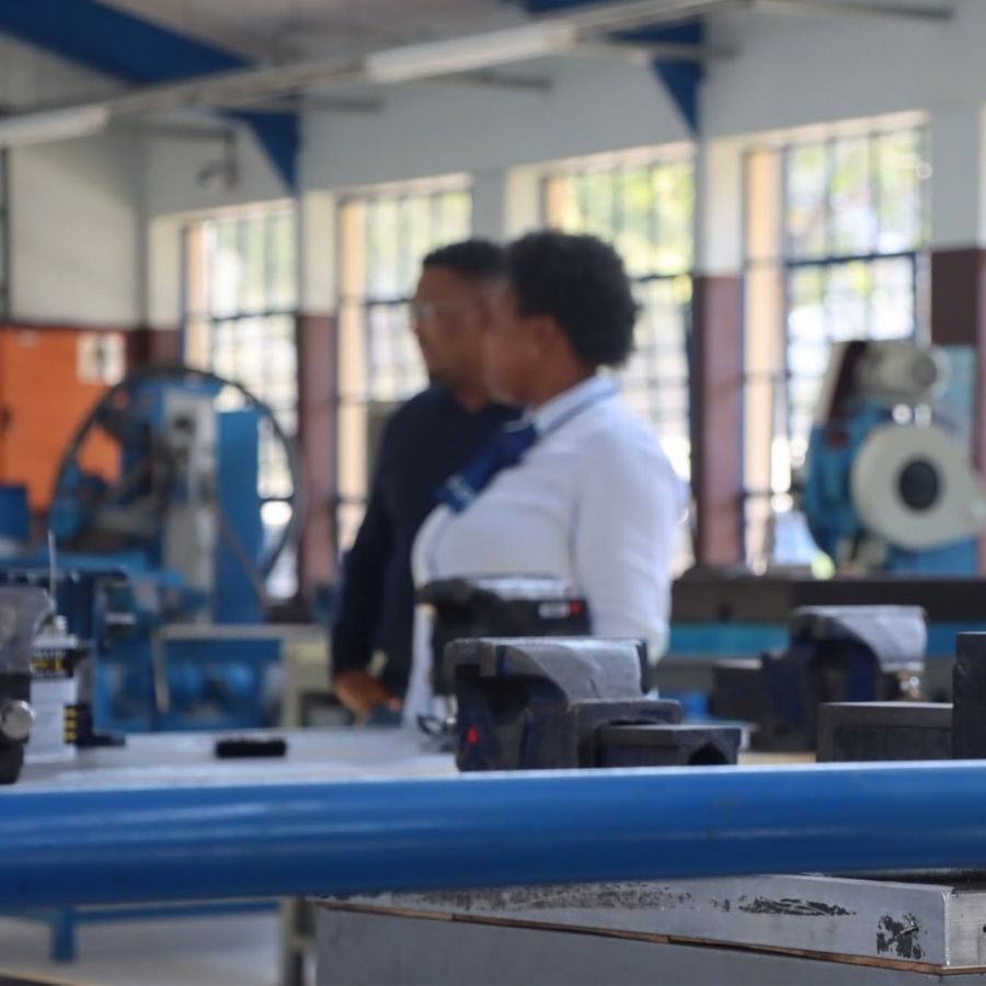 Blurred view of two people walking through the Tshwane South TVET College mechanical engineering workshop with vices and machinery