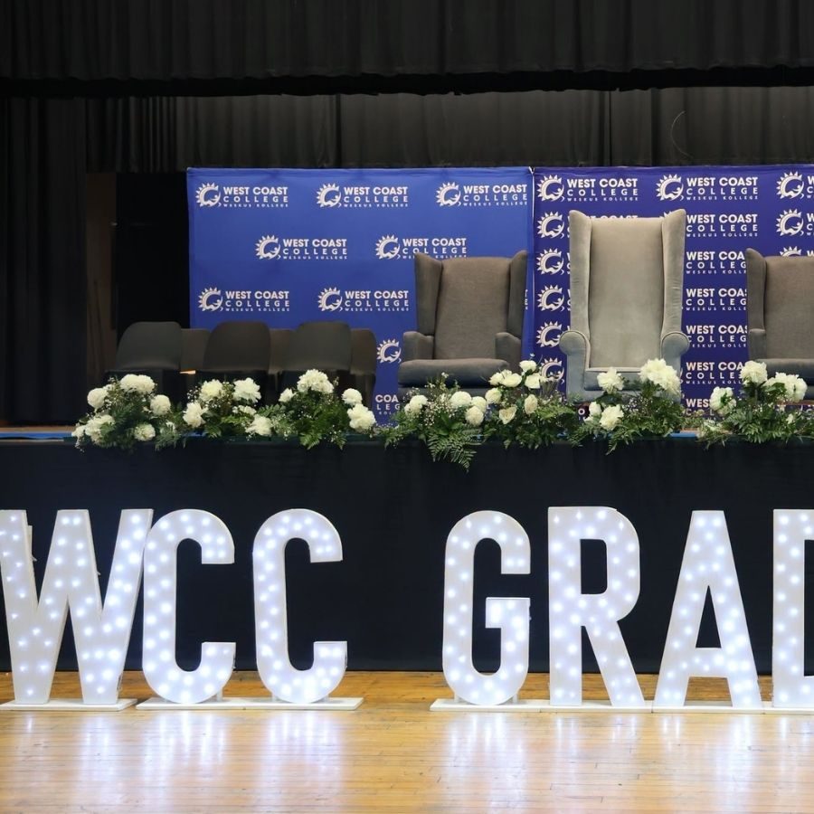 West Coast College Graduation Ceremony Stage Setup Stage decorated with "WCC GRAD" marquee letters, floral arrangements, and West Coast College banners ahead of a graduation ceremony