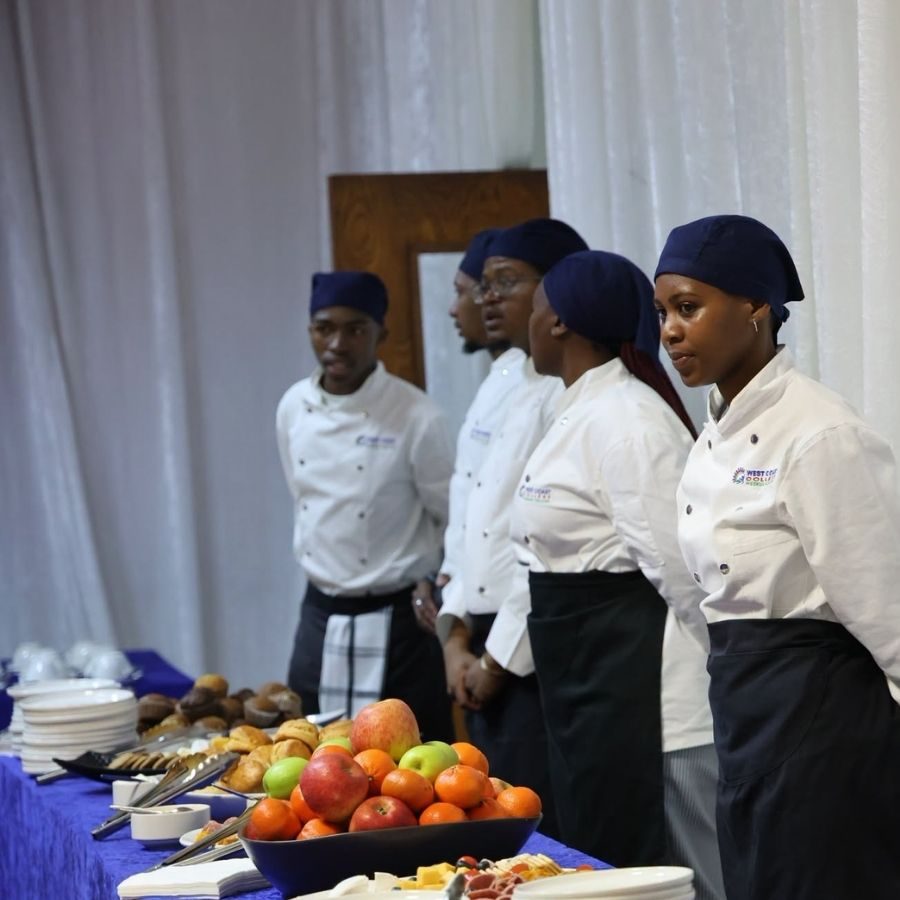 West Coast College Hospitality Students Serve at Event West Coast TVET College hospitality students in chef uniforms stand beside a catering table of fruit and pastries at a college event